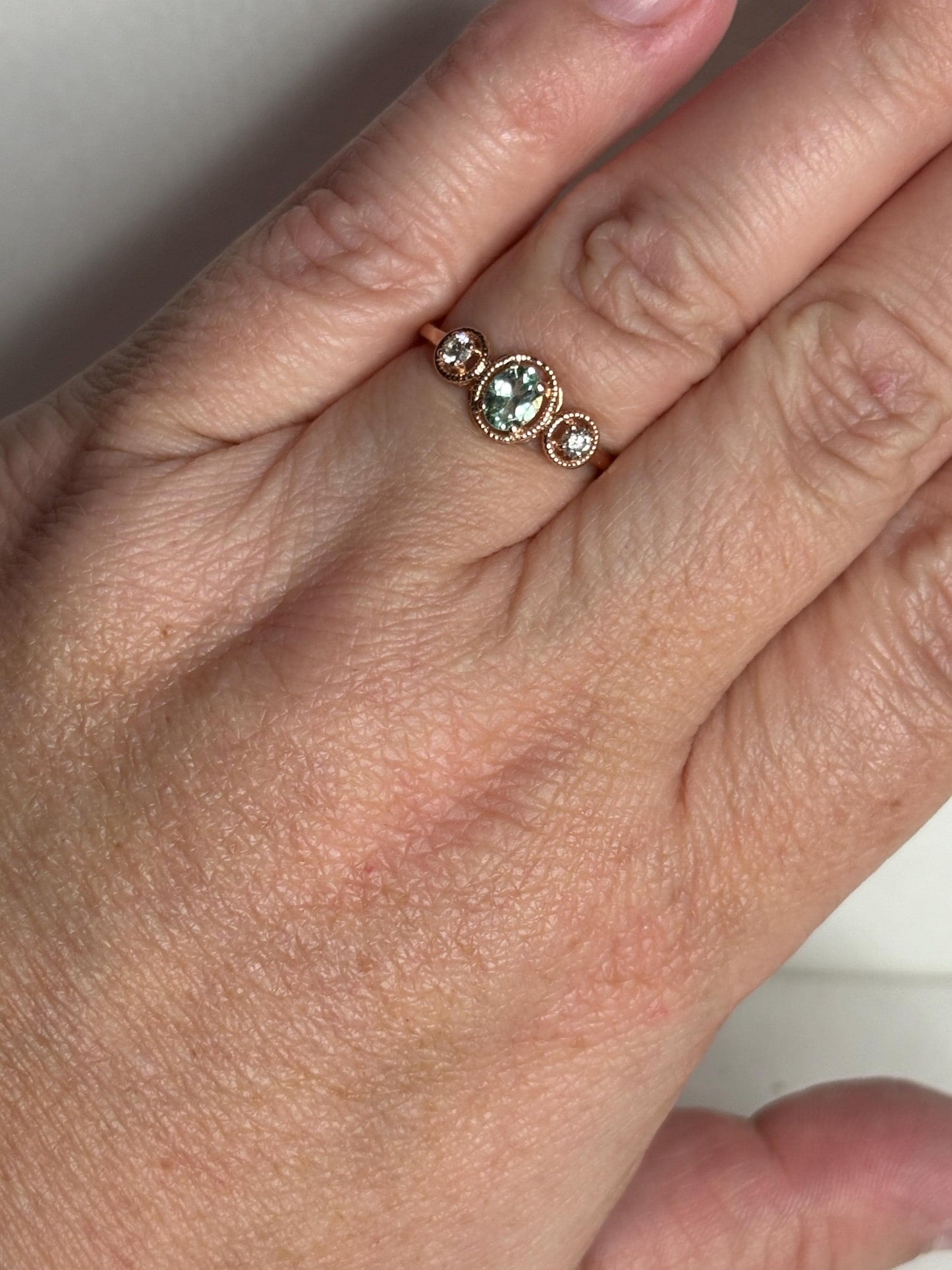 A 14k rose gold ring with a central oval mint green tourmaline and two side diamonds.