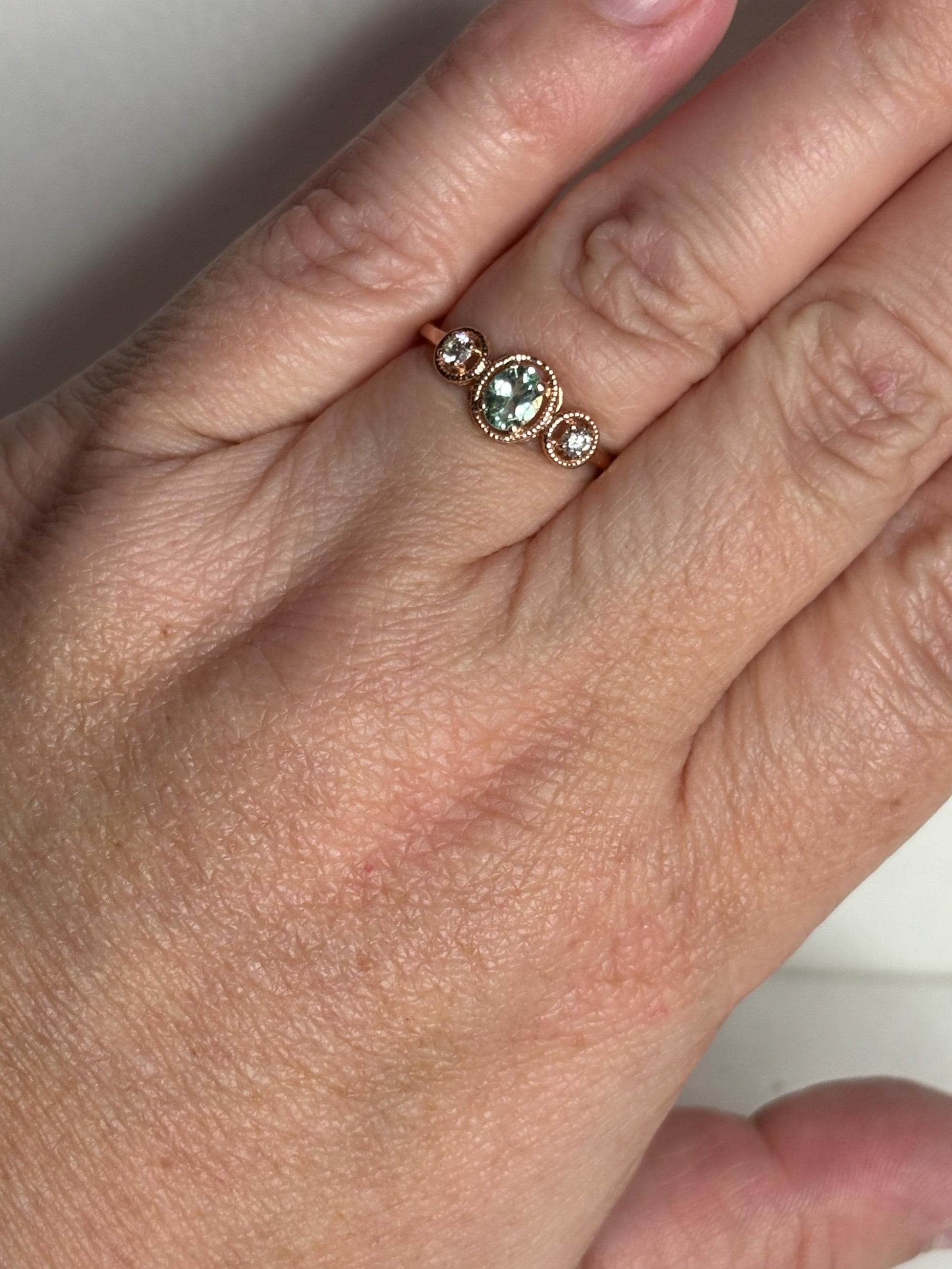 A 14k rose gold ring with a central oval mint green tourmaline and two side diamonds.