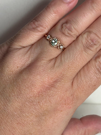 A 14k rose gold ring with a central oval mint green tourmaline and two side diamonds.