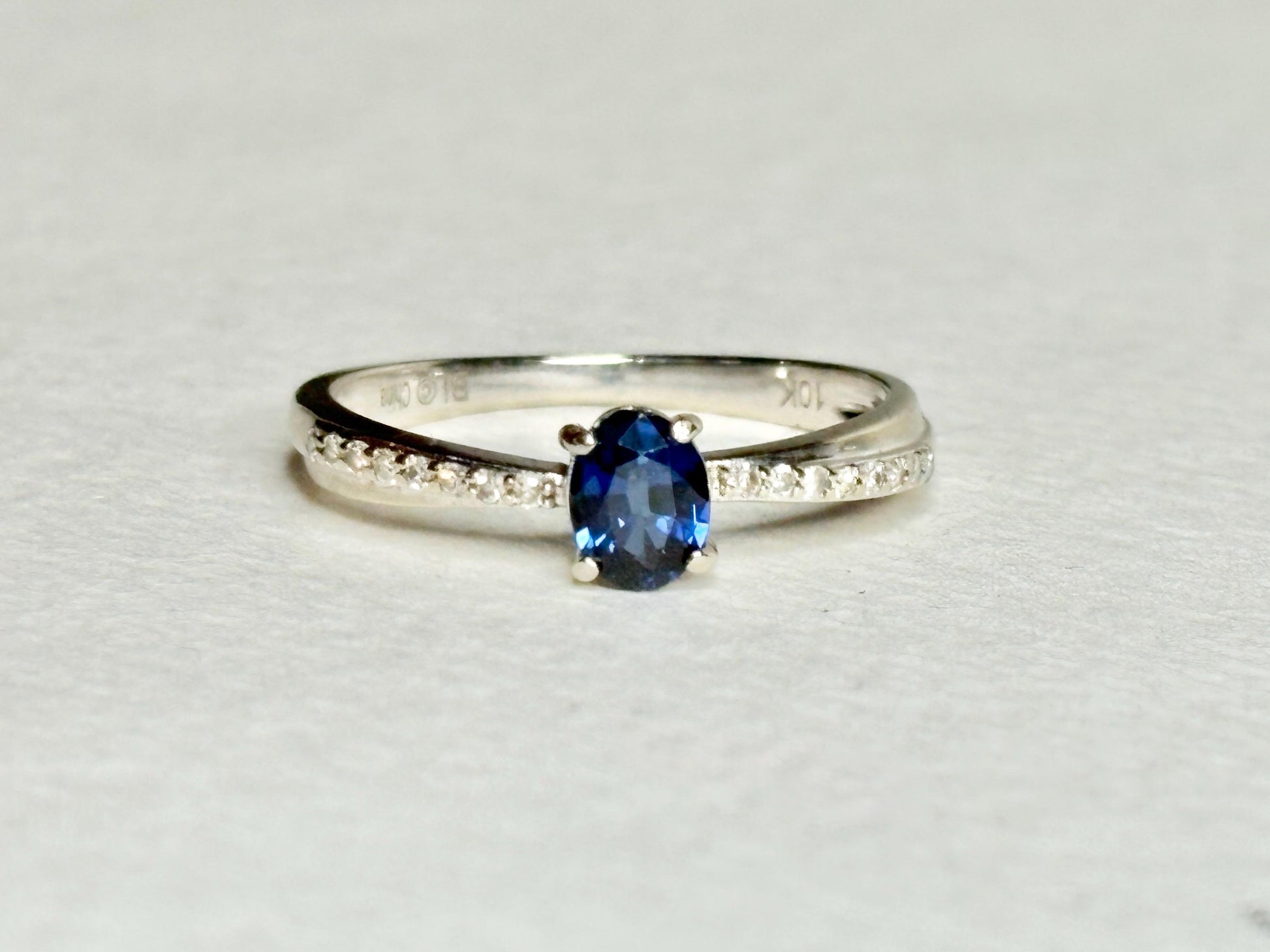 10k white gold ring with oval blue sapphire and diamond accents.