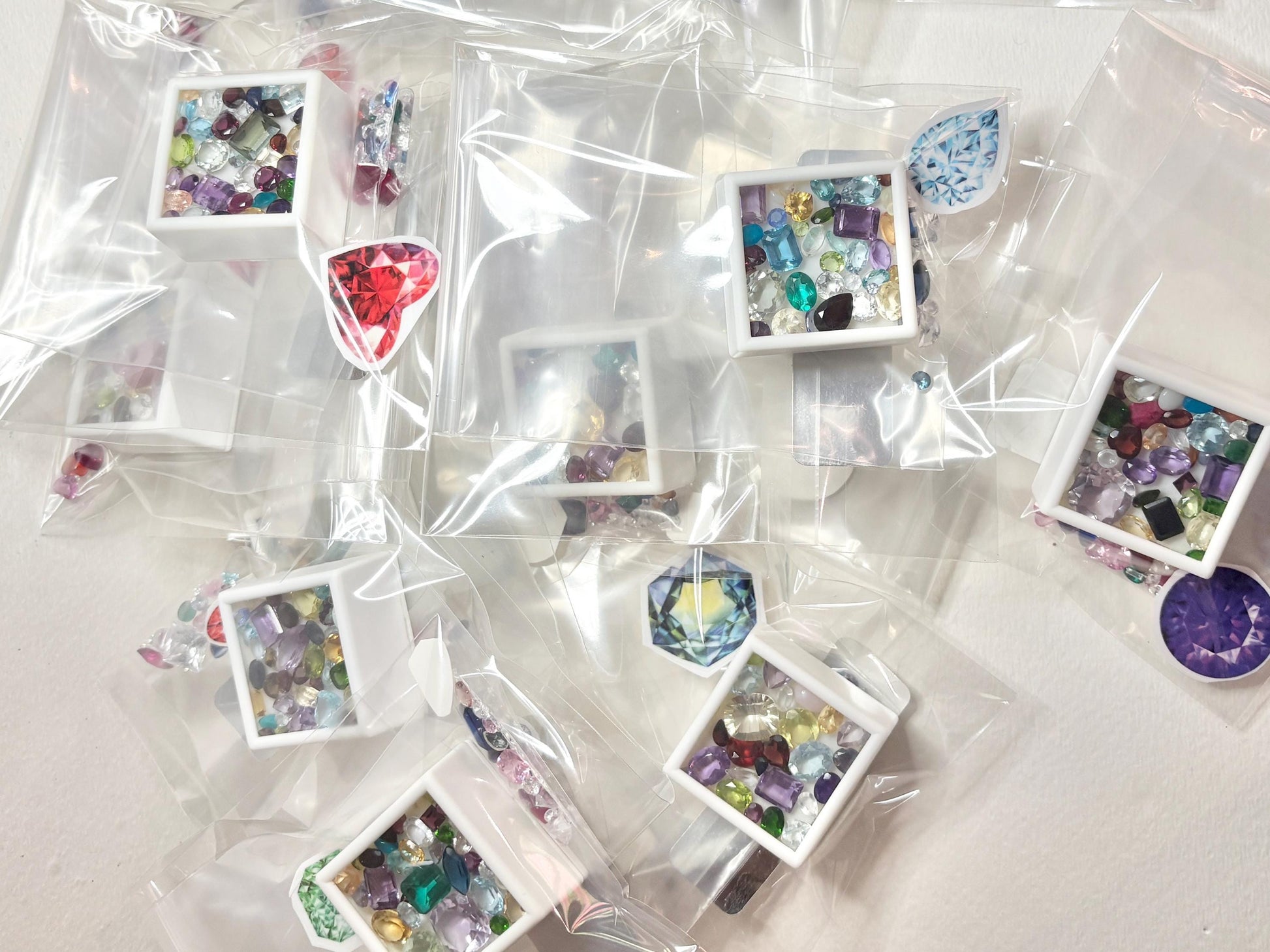 A collection of mixed faceted and cabochon gemstones in plastic packaging.