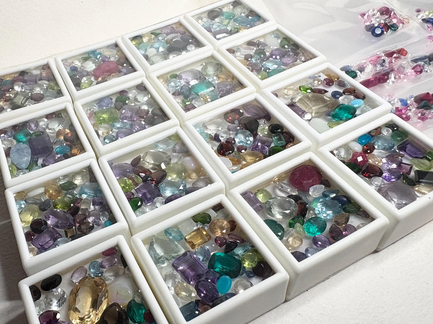A parcel of mixed faceted natural and synthetic gemstones in white display trays.