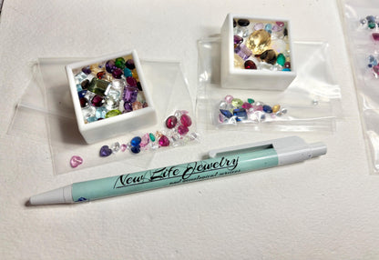 A collection of mixed faceted natural and synthetic gemstones in parcels and a white tray.