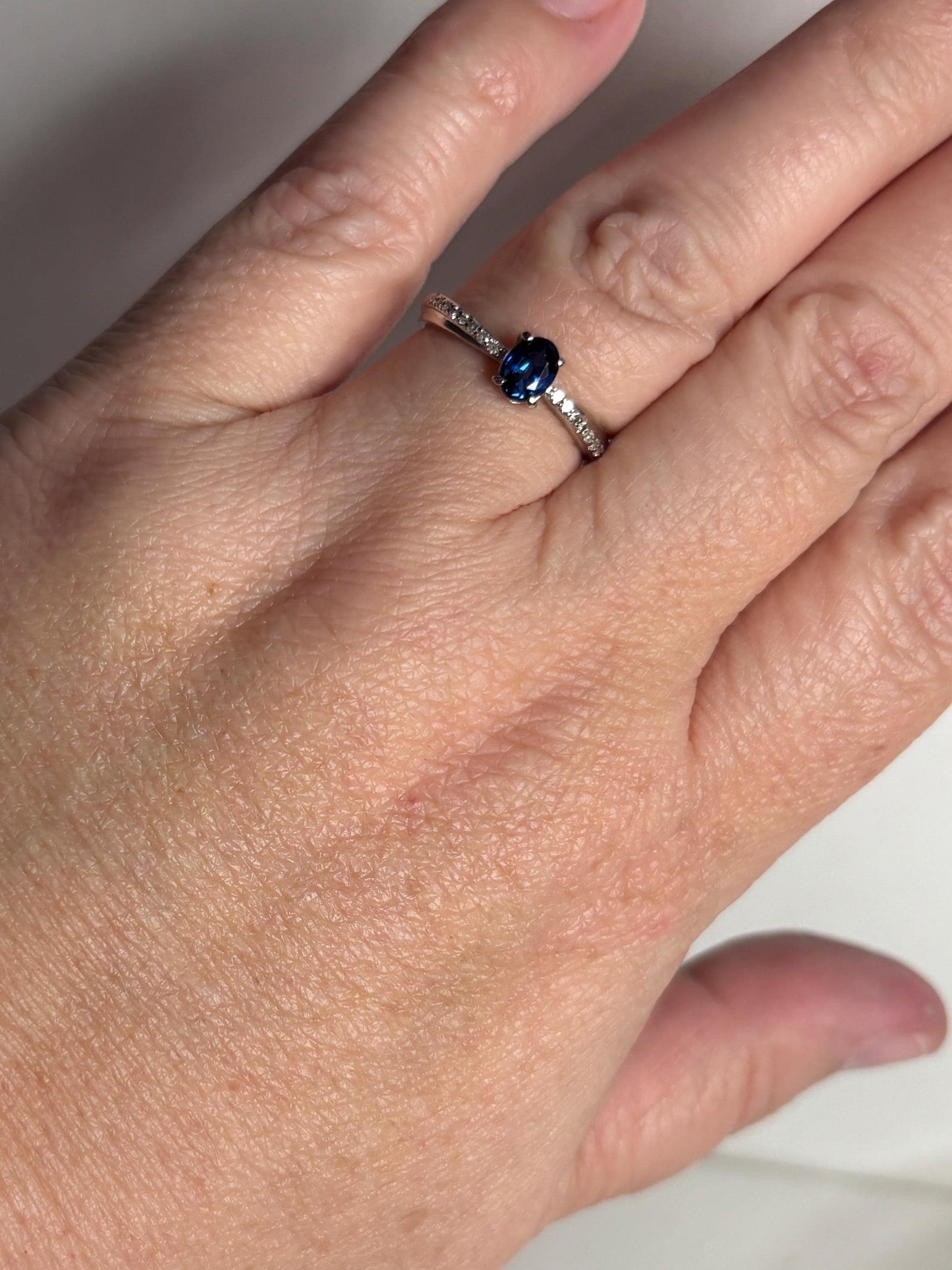Oval blue sapphire and diamond crossover band ring in 10k gold.